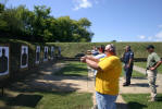 Instructors stand behind as students fire their weapons at the firing range.